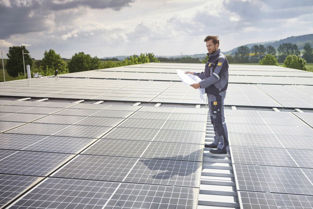 Elektroniker steht mit Plan auf Photovoltaik Anlage
