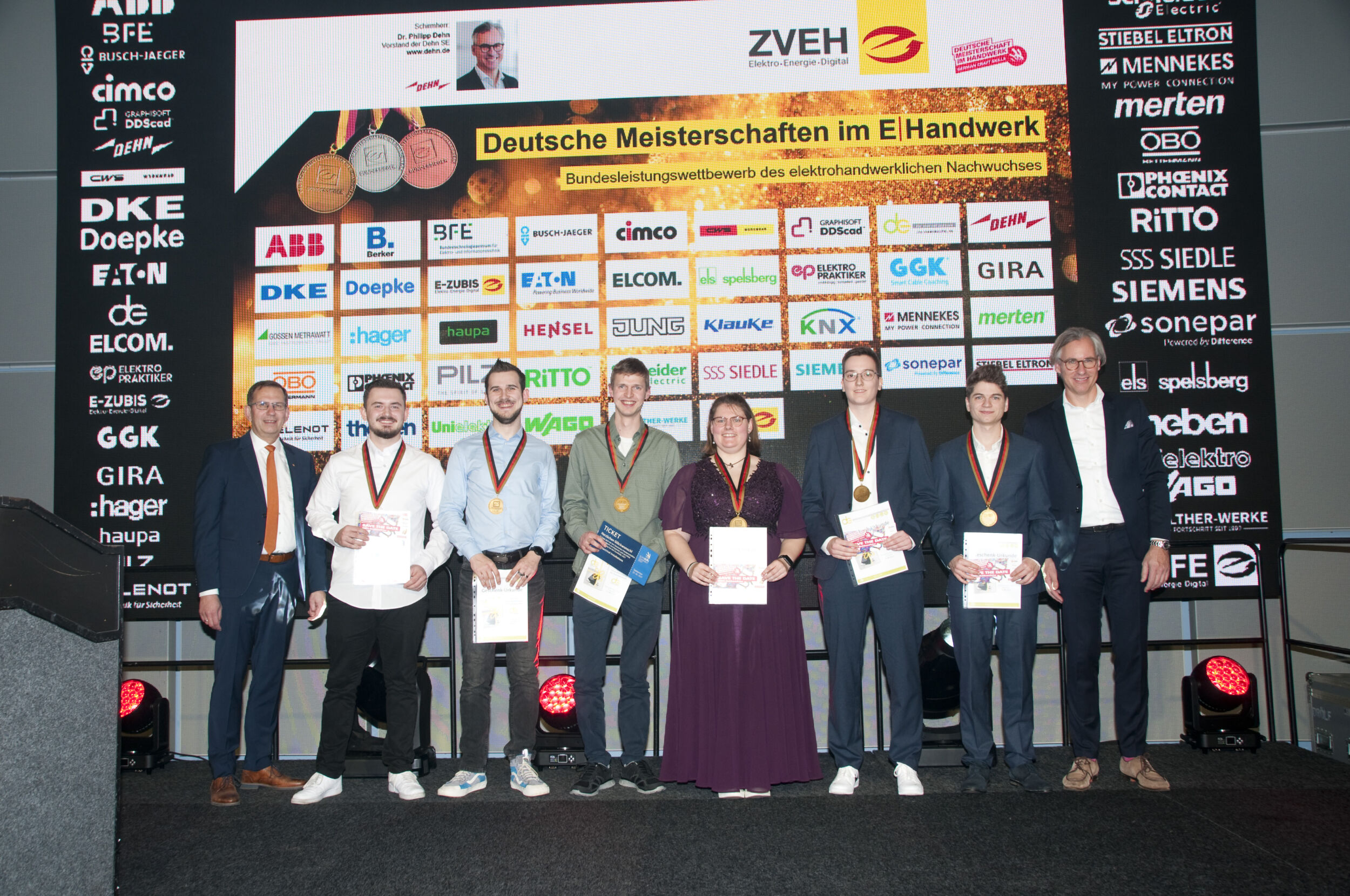 ZVEH-Vizepräsident Karsten Krügener, Marcel Küst (Elektroniker für Maschinen und Antriebstechnik), Tobias Wieland (Elektroniker für Gebäudesystemintegration), Linus Emmering (Elektroniker Fachrichtung Energie- und Gebäudetechnik), Cara Enders (Informationselektronikerin Einsatzgebiet: Gefahrenmelde- und Telekommunikationstechnik), Lara Wenskowski (Elektronikerin Fachrichtung Automatisierungs- und Systemtechnik), Peter Südmersen (Informationselektroniker Einsatzgebiet: Büro- und Breitbandtechnik) und der DMH-Schirmherr 2025, Dr. Philipp Dehn.