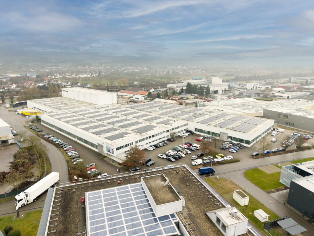 Die rund 3.410 PV-Module auf dem B&uuml;rogeb&auml;ude (im Vordergrund) und den Werkhallen erzeugen j&auml;hrlich etwa 1.500 Megawattstunden gr&uuml;nen Strom. Davon profitiert auch der Einsatz des E-Trucks in Kooperation mit dem Dachser Logistikzentrum Karlsruhe. - Bild: ABB