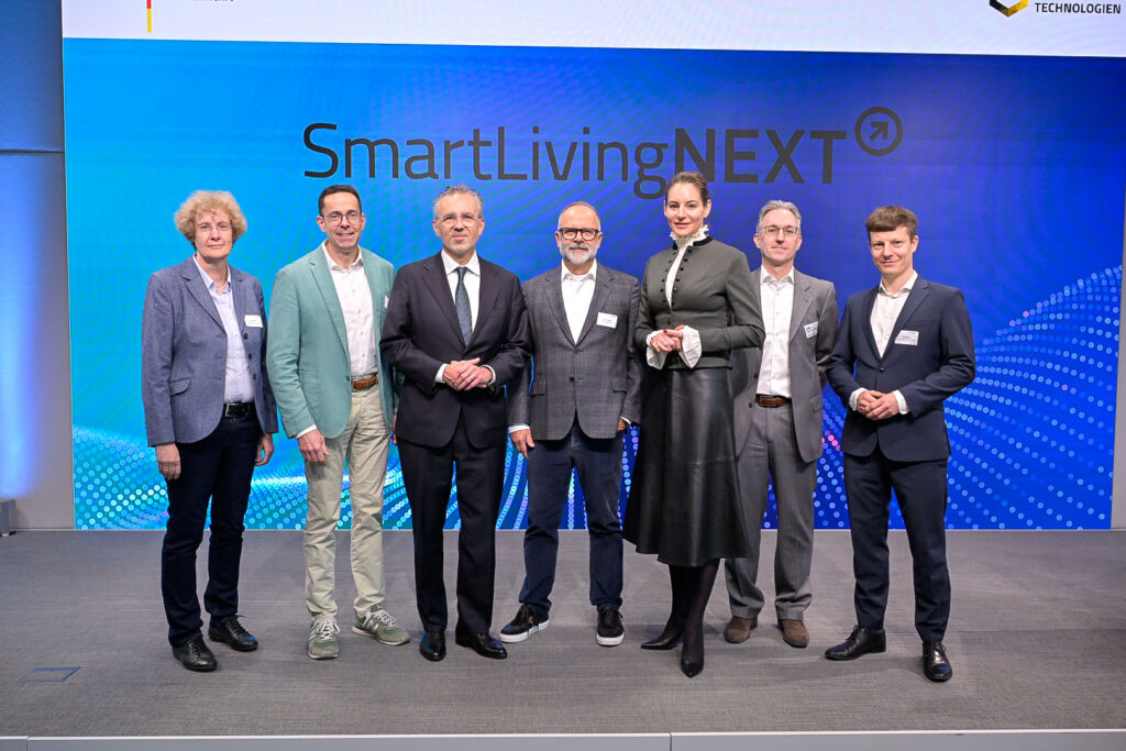 Diskutierten auf der SmartLivingNEXT-Konferenz im Forum Digitale Technologien in Berlin &uuml;ber den Start in den Realbetrieb: Ute Bernhardt, Leiterin des Referats K&uuml;nstliche Intelligenz im Bundesministerium f&uuml;r Forschung, Technologie und Raumfahrt (BMFTR), Wolfgang Weber, Vorsitzender der ZVEI-Gesch&auml;ftsf&uuml;hrung, Thomas Jarzombek, Parlamentarische Staatssekret&auml;r beim Bundesminister f&uuml;r Digitales und Staatsmodernisierung, Michael Schidlack, Principal Researcher bei der Forschungsvereinigung Elektrotechnik beim ZVEI e. V. und Projektleitung des SmartLivingNEXT Leitprojekts, Dr. Alexandra-Gwyn Paetz, Abteilungsleiterin Technologische Souver&auml;nit&auml;t & Innovation, Bundesministerium f&uuml;r Forschung, Technologie und Raumfahrt (BMFTR), Matthias Szymansky, Kompetenzzentrumsleiter Analytics & AI bei Materna Information & Communications SE, Filip Milojkovic, Teamleiter Data Management & AI bei Materna Information & Communications SE (v. l.).