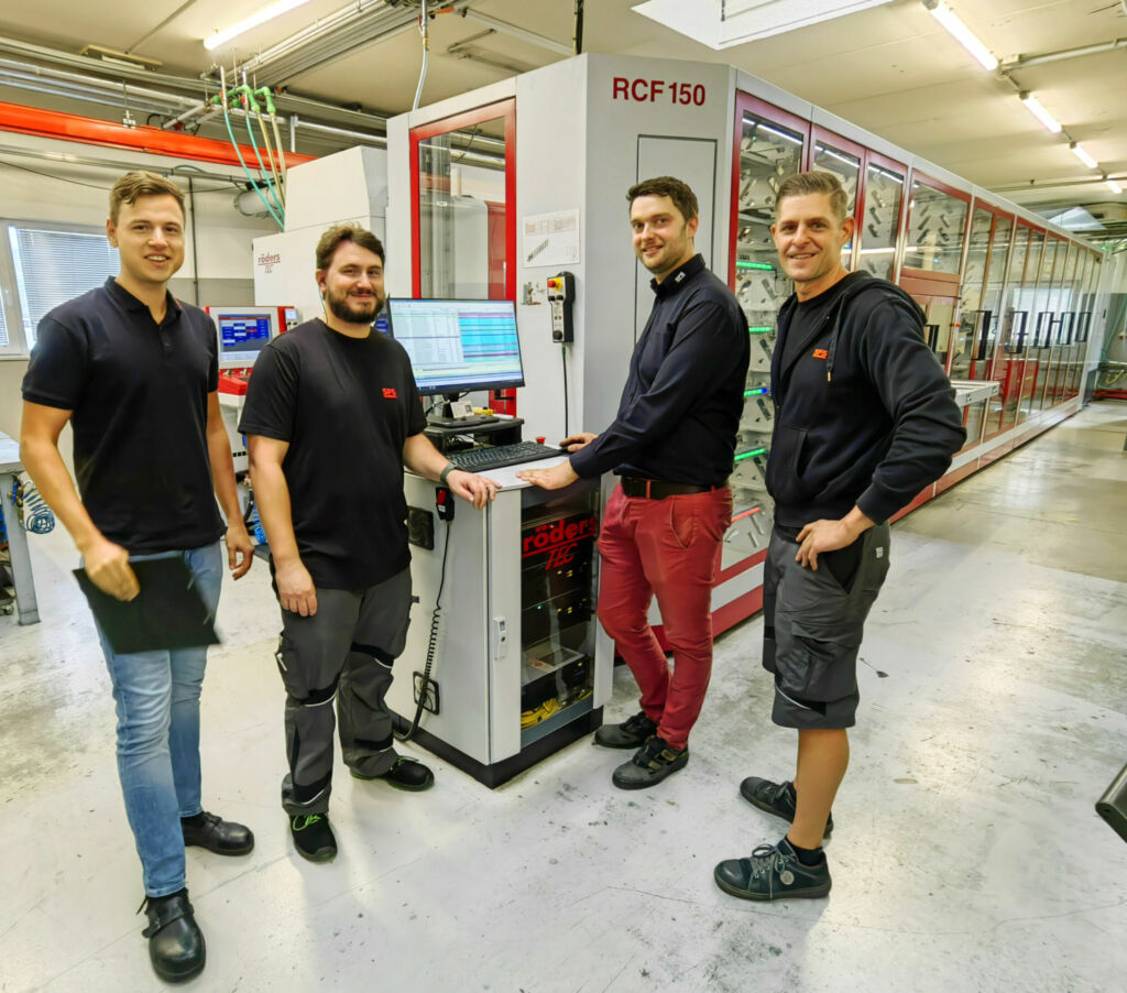 Freuen sich &uuml;ber &sbquo;ihre&lsquo; R&ouml;ders-Fertigungslinie (v.l.): Jakob Kaiser (Arbeitsvorbereitung), Friedrich Georg (CAM/Fr&auml;sen), Heinrich Ruckenbauer (Leiter Werkzeugbau) und Mario Kreutzer (CAM/Elektrodenfr&auml;sen) &ndash; vorne das Jobmanagementsystem RMSMain, hinter den Glasfronten die Regale f&uuml;r Werkzeuge und Paletten. Die Bearbeitungssysteme sind auf der R&uuml;ckseite aufgereiht. 