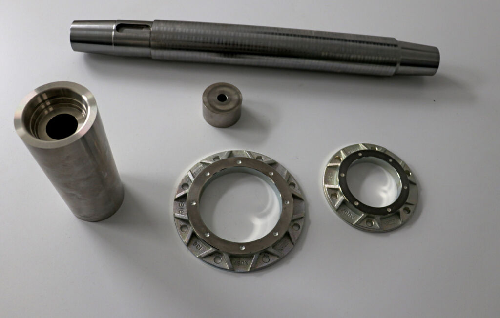 Typische auf der Index B400 bearbeitete Teile: oben eine Antriebswelle mit Passfedernut und beidseitigem Gewinde; links eine Kühlkokille für eine Aluminiumgießerei, die auf der Index G250 vorbearbeitet wird und dann auf der Index B400 mit Reitstockfunktion den Außendurchmesser komplett überdreht bekommt; in der Mitte ein Kolben für eine Vakuumpumpe (besonders anspruchsvoll wegen hoher Form- und Lagetoleranzen sowie innenliegender präziser Passung; unten rechts in OP10 und OP20 bearbeitete Gussteile für Tragarmsysteme.