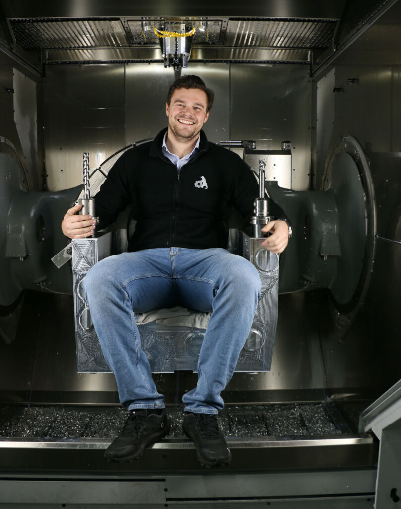 Weil das eingespannte Bauteil ihn an ein Sitzm&ouml;bel erinnert, nimmt der Gesch&auml;ftsleiter Sebastian Behr kurzerhand im Arbeitsraum der Hermle C 62 U MT darauf Platz. In seinen H&auml;nden die beiden Werkzeuge von Ingersoll. 