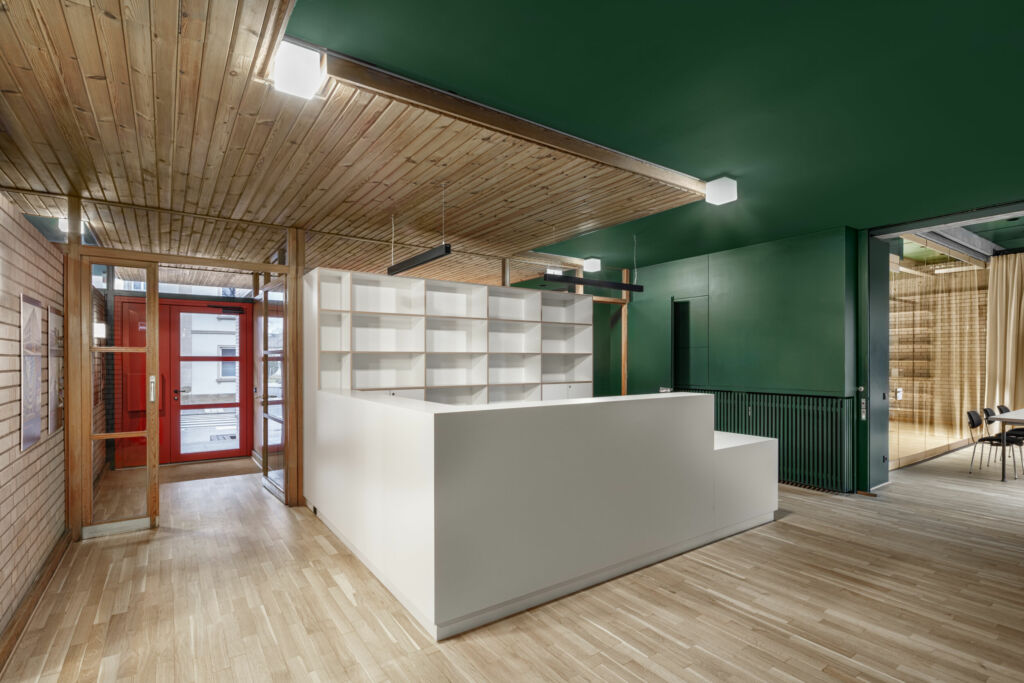 Neue Arbeit im alten Gemeindehaus 5 Als neues Element gliedert die weiße Rezeption den Eingangsbereich. Dahinter schirmt die Trennwandanlage den Besprechungsraum vom Großraumbüro ab.