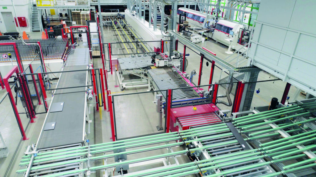 Effizient zum Kundenwunsch 1 Anlage für Badmöbelfertigung: Plattensägen und Kantenbearbeitungsanlage sind über eine Riemenförderstrecke und einen Rechenpuffer verbunden.