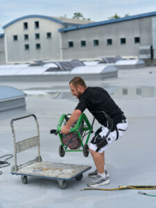 Ein Mitarbeiter von Schühle Abdichtungen nutzt das Exoskelett IX Back Air zur Rückenentlastung beim Heben schwerer Lasten. - Bild: Suitx by Ottobock
