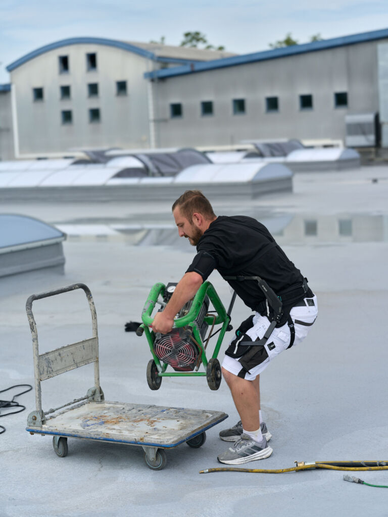 Ein Mitarbeiter von Schühle Abdichtungen nutzt das Exoskelett IX Back Air zur Rückenentlastung beim Heben schwerer Lasten. - Bild: Suitx by Ottobock