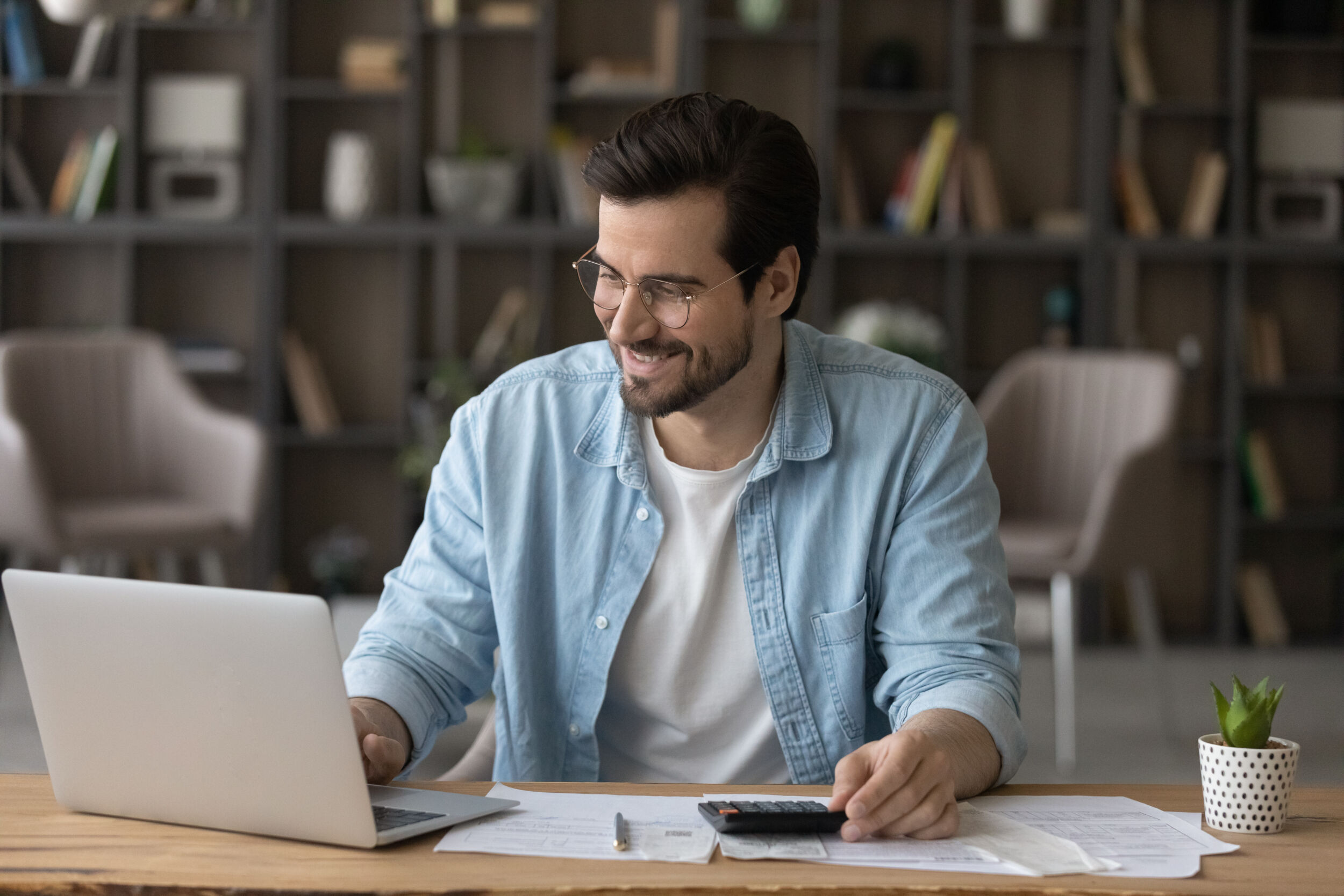 Smiling businessman in glasses using laptop calculating bills managing finances