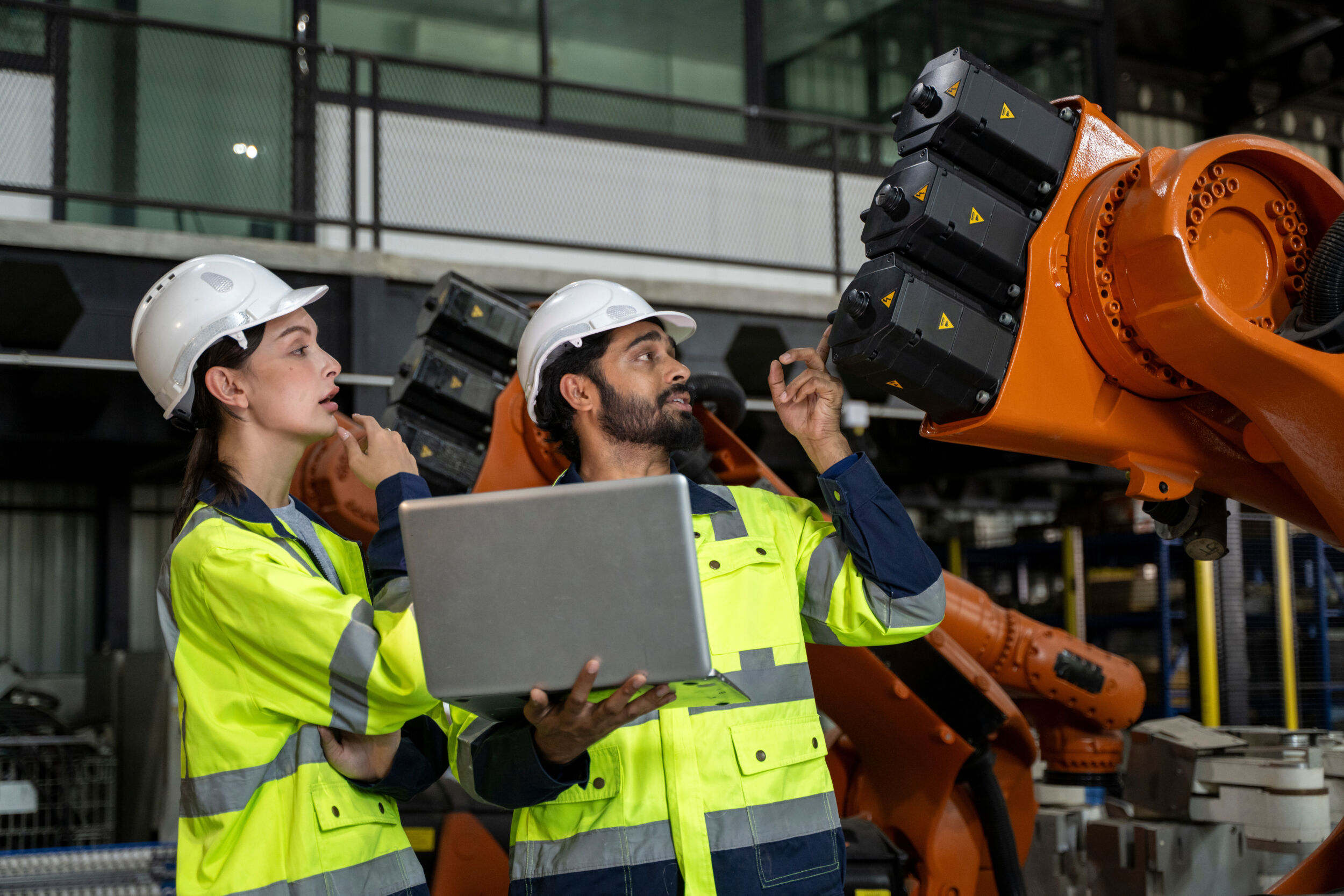 Two engineers discussing robotic arm programming using a laptop in a smart factory
