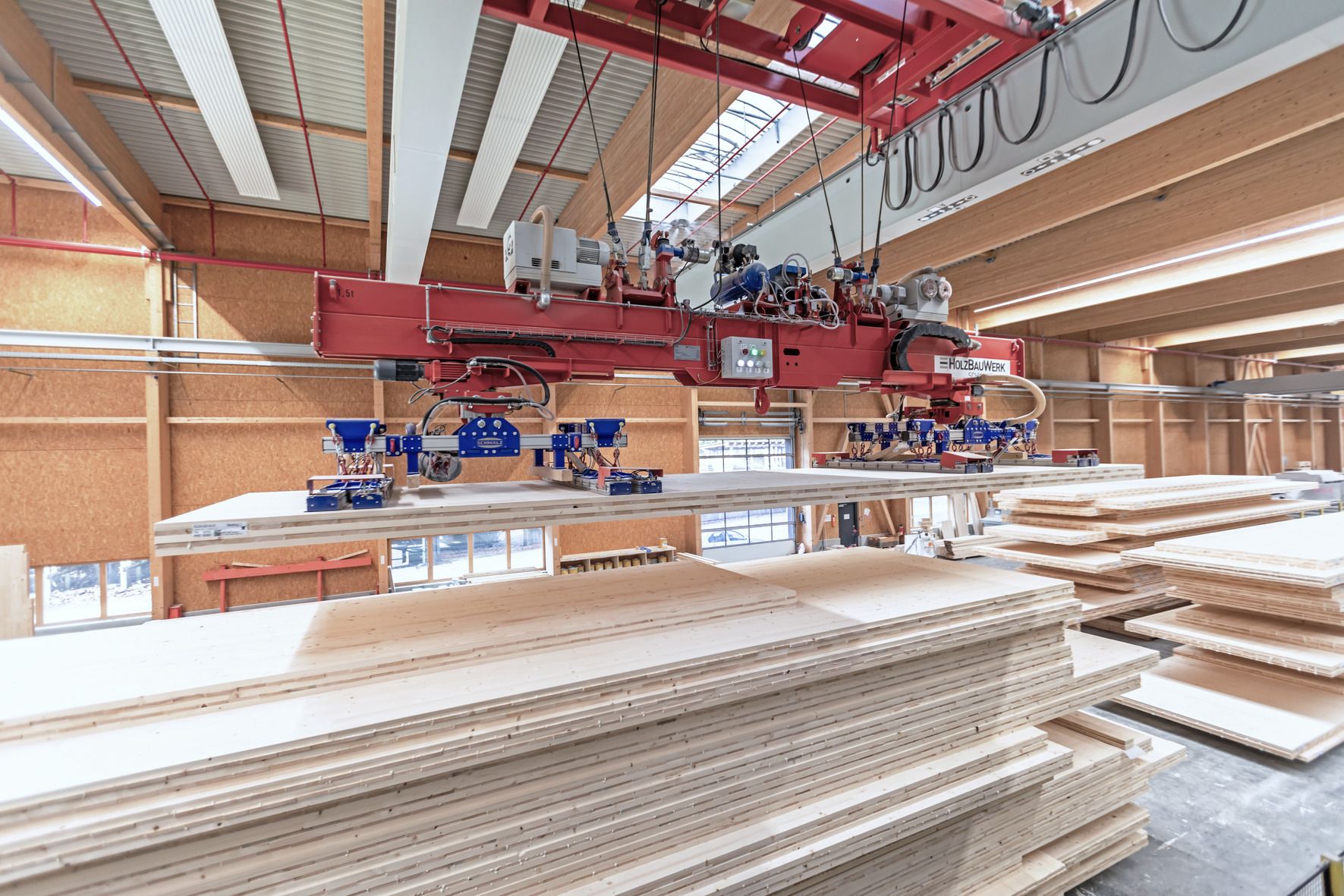 Zwei Saugspinnen an einem Deckenkran stapeln die Brettsperrholzplatten bis zur weiteren Verwendung oder führen sie den nächsten Bearbeitungsschritten zu.