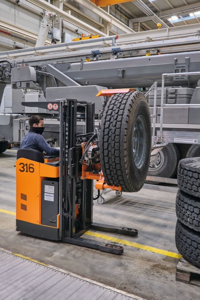 Mit dem Elektro-Geh-Hochhubwagen - hier als Fahrersitz-Ausführung - werden Reifen oder andere Baumaschinenteile aufgenommen.