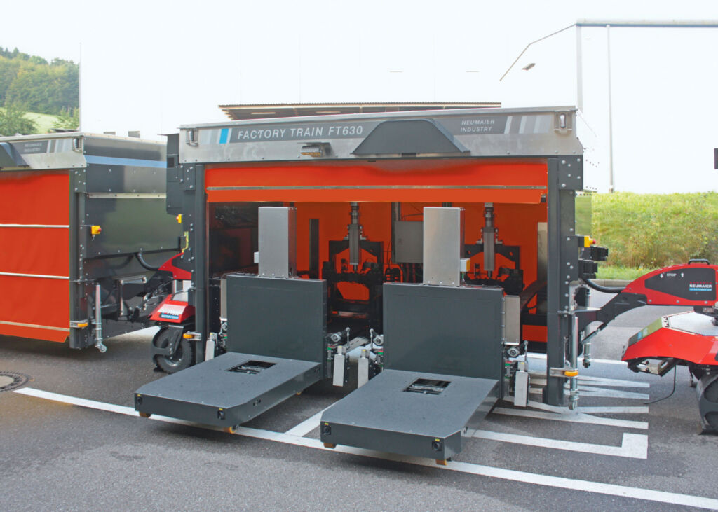 Vollautomatisierter und autonomer Outdoor-Routenzug Factory Train FT630 von Neumaier Industry mit Teleskopgabel-Warenträger für die automatisierte Aufnahme und Abgabe von Ladungsträgern auf/von Übergabestationen oder direkt auf den bzw. vom Boden.