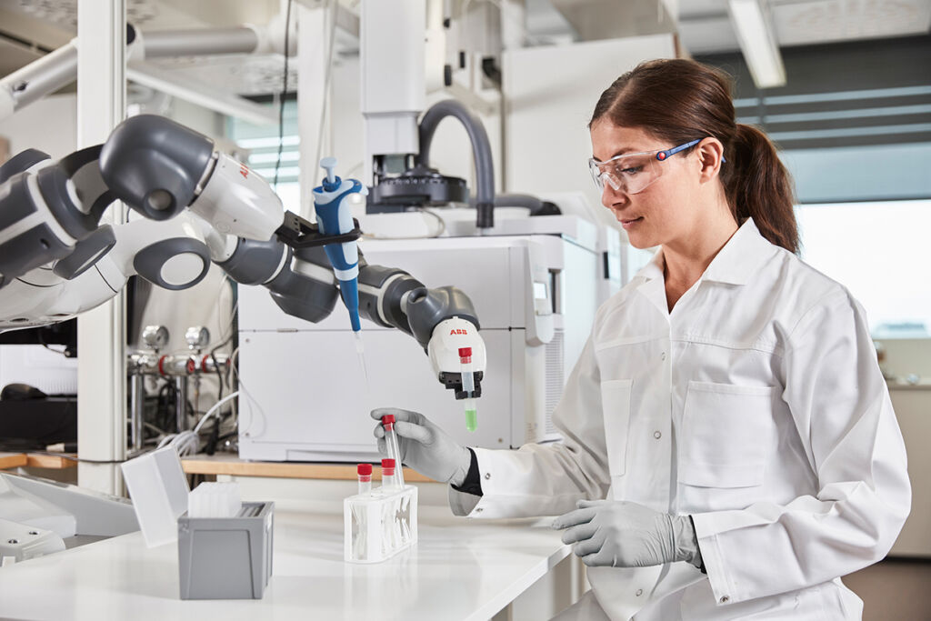 ABB-Cobots für neue Branchen und Märkte 1 Eine Frau arbeitet in einem Labor mit einem Roboter und nimmt gemeinsam mit ihm Proben.