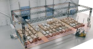 Im Wareneingang überspannt der Seilroboter zwei Containertore samt Stellfläche. Ein Förderband führt die Packstücke aus dem Container in den Arbeitsraum, der Roboter setzt sie auf rund 60 Zielpaletten ab, die ohne Gassen dicht an dicht stehen.