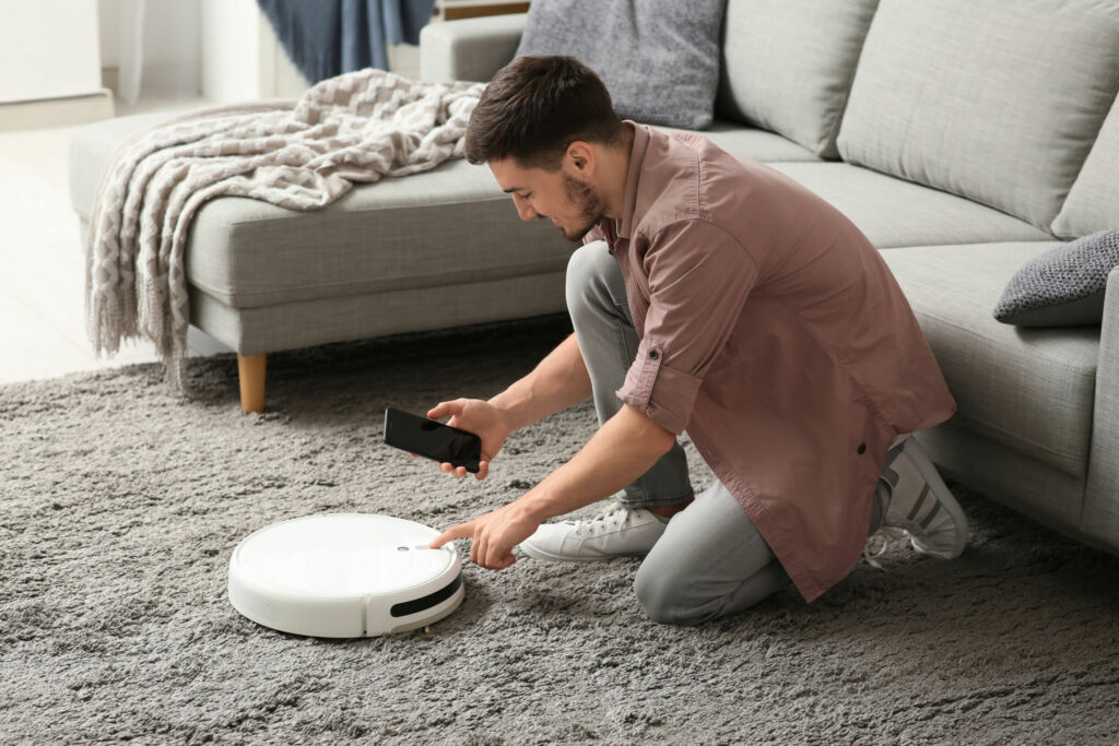 BSI sieht Cybersicherheit durch CRA signifikant gestärkt 1 Young man with mobile phone turning on modern robot vacuum cleaner at home