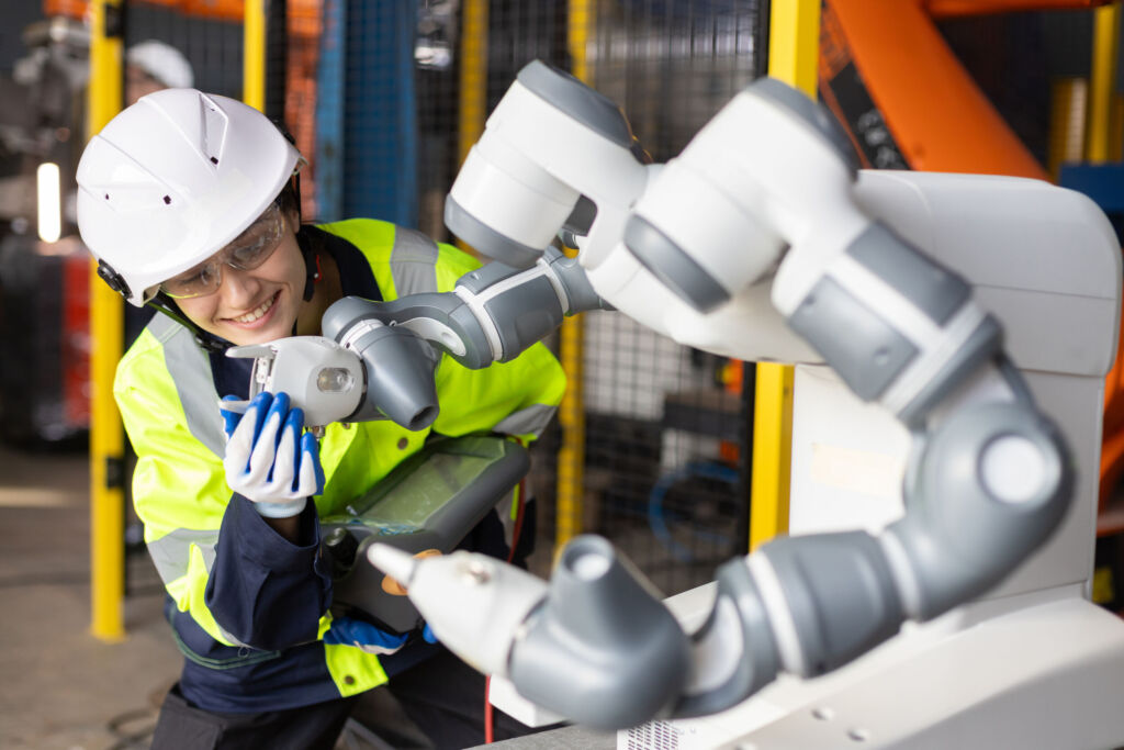 Universal Robots befragt Fachkräfte zum Thema Cobots 1 Female engineer operating collaborative robot in smart factory smiling while adjusting robotic arm. Concept of cobot technology automation Industry 4.0 and human robot interaction