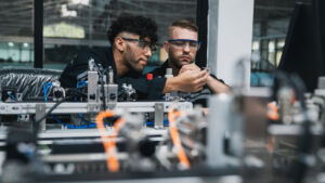 Studie: Firmen übergehen Geflüchtete bei der Ausbildungsplatz-Vergabe 1 Student engineer Assembling Robotic Arm with computer in Technology Workshop. Service Engineer Holding Robot Controller and Checking Robotic Arm Welding Hardware