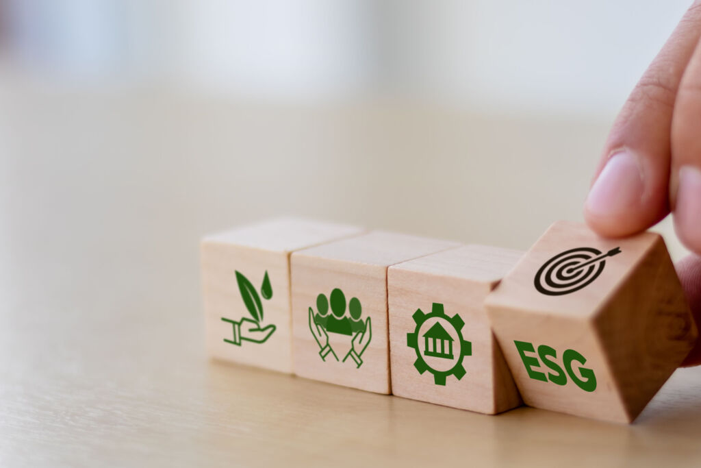 Mit IoT-Technologie zum Nachhaltigkeits-Reporting 1 ESG concept of environmental, social and governance. Sustainable corporation development. Hand flips wooden cubes with target setting to ESG icon with other ESG icons on bright background.Copy space.