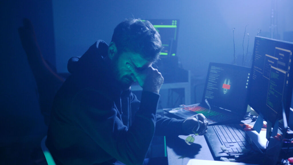 Cyberangriffe werden professioneller 1 Profile of stressed hacker trying a virus attack on corporate servers in dark place. Night hacking fail in the office