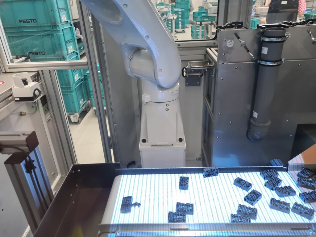 Die zuzuführenden Bauteile in den ungefähren Abmessungen einer Streichholzschachtel werden in einen Bauteilbunker gekippt, von dort über einen Steigförderer auf ein Förderbandsystem gebracht und landen auf einem Band im Erkennungsbereich des 3D-Bildverarbeitungsystems.